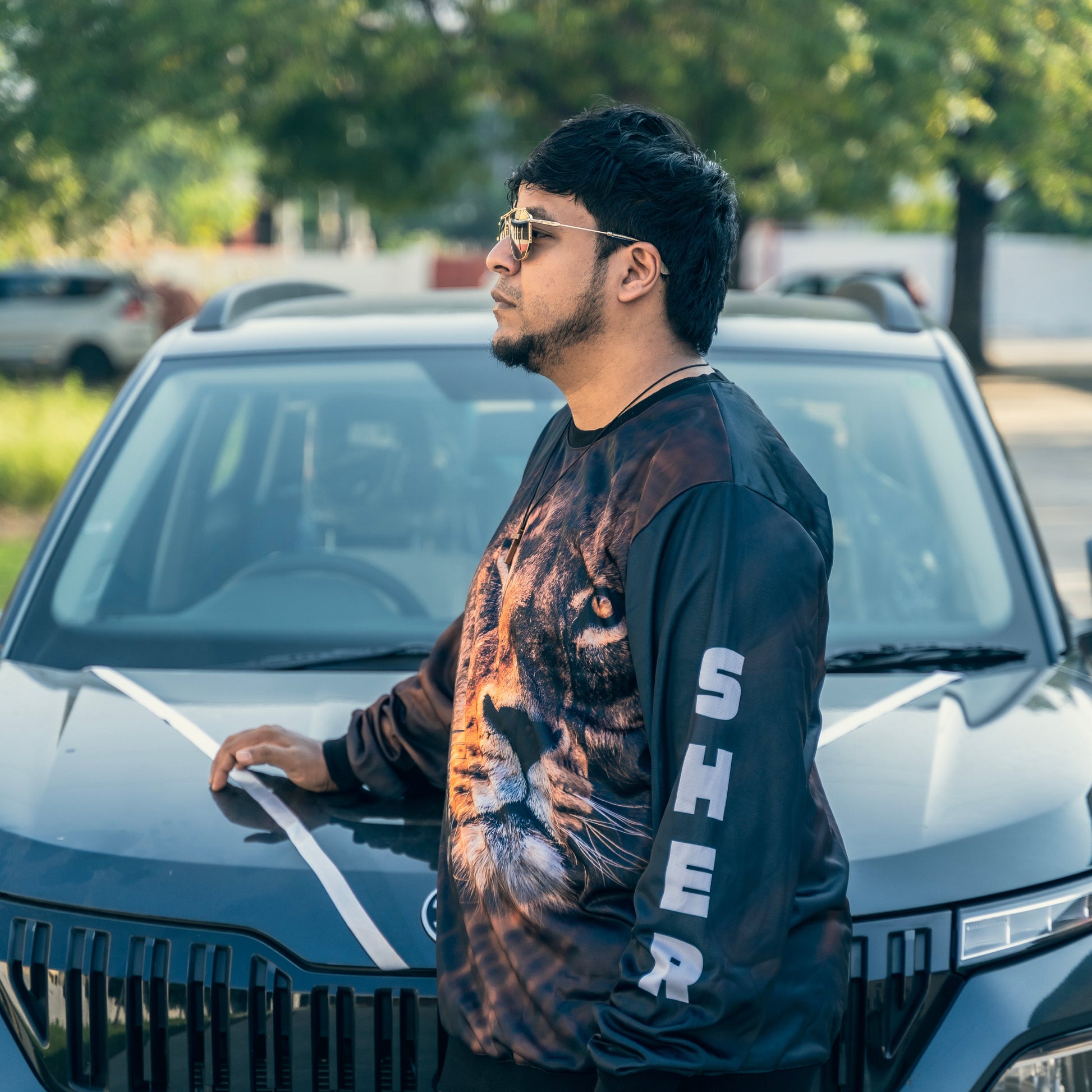 Man standing next to a car wearing a black and orange graphic sweatshirt.